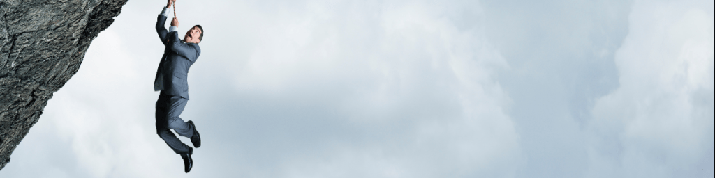 Man holding onto a rope that is suspended from the edge of a clif