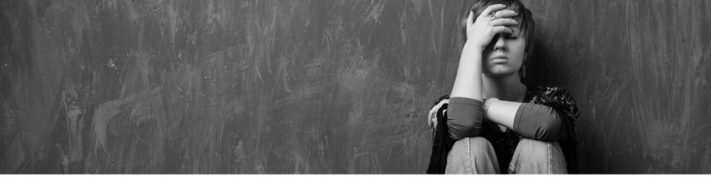 Woman sitting with her hand over her forehead and eyes, in grief and sadness. 