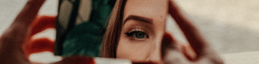 Person looking at their reflection in a small handheld mirror.
www.healinglight.blog