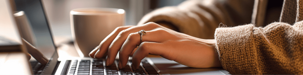 Person typing at a laptop with a cup of coffee in the background.